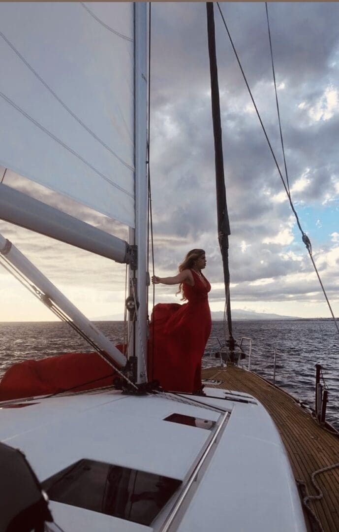A woman in red dress standing on the side of a boat.