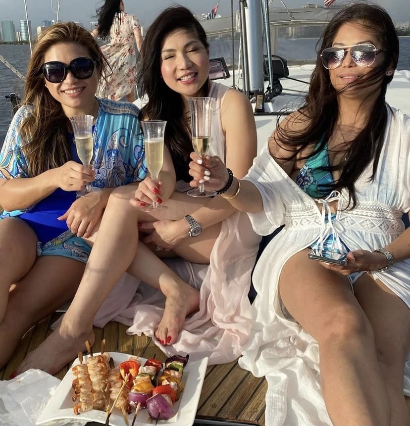 Three women sitting on a deck holding champagne.