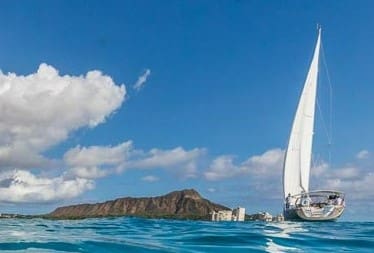 A sailboat in the ocean with mountains behind it.