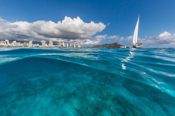 A sailboat in the ocean with buildings and clouds